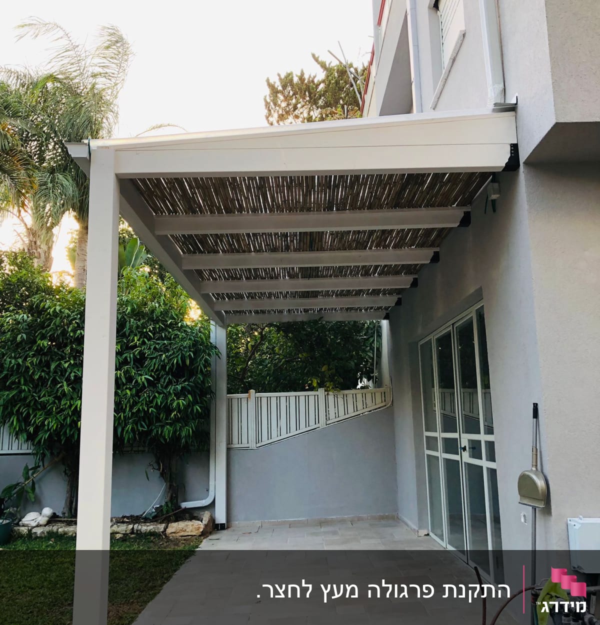 פרגולה מעץ עם גג קנים מעל מרפסת מרוצפת